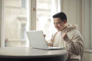 happy asian man raising two hands in front of a laptop